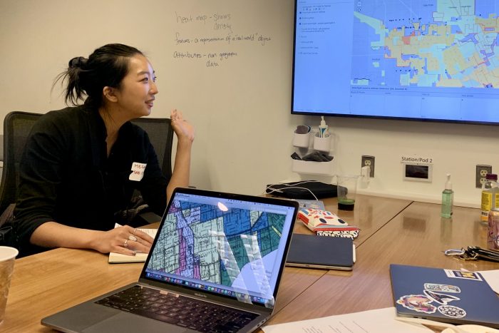 Asian woman sitting at table looking at map on wall screen.