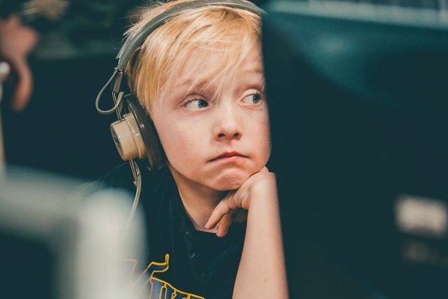 boy wearing headphones, sitting behind computer