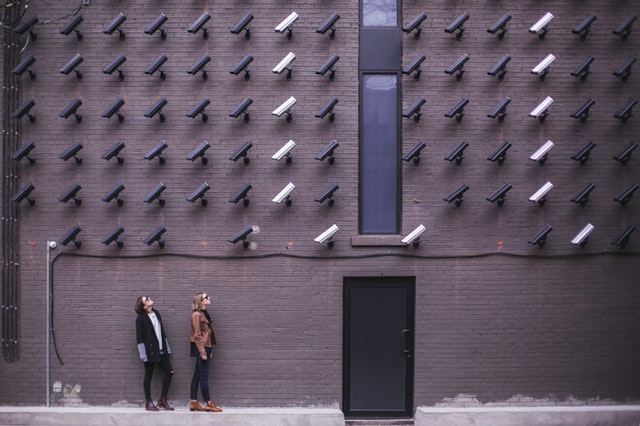 two women by a wall with many CCTV cameras focused on them