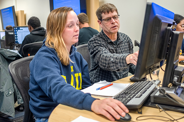 Female student and male instructor siting at computer, working.