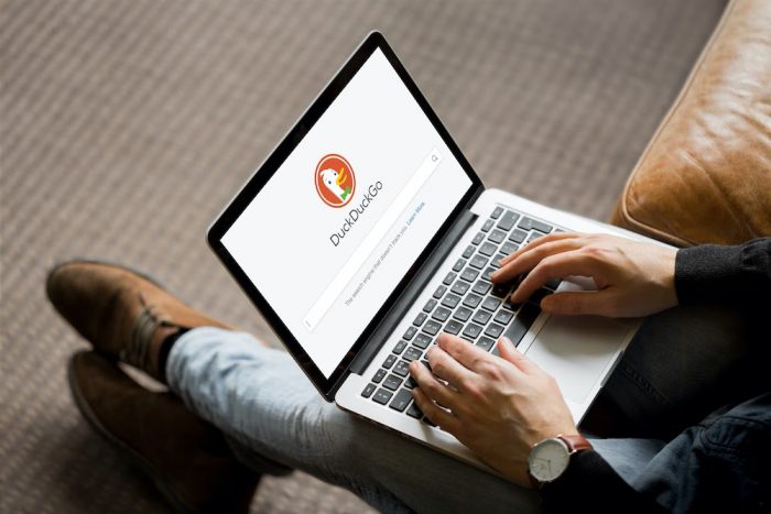 Man holding laptop with DuckDuckGo on screen.