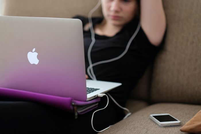 young woman on a sofa wearing earbuds and working on a laptop