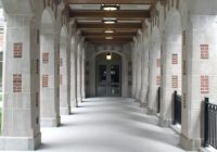 (Photo of a concrete walkway lined by columns leading to doors to a building.)