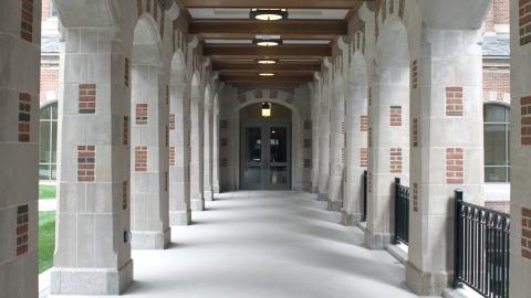 (Photo of a concrete walkway lined by columns leading to doors to a building.)
