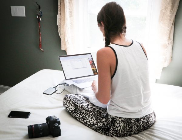A woman sits on a bed with her laptop.