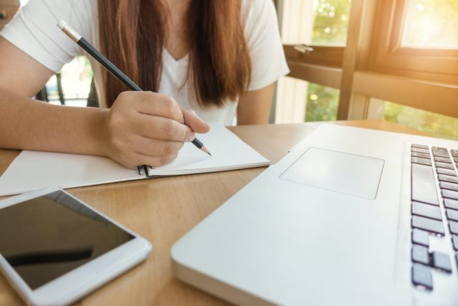young woman at computer writing in notebook