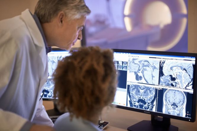 Man and woman in lab coats viewing MRI images on computer monitor