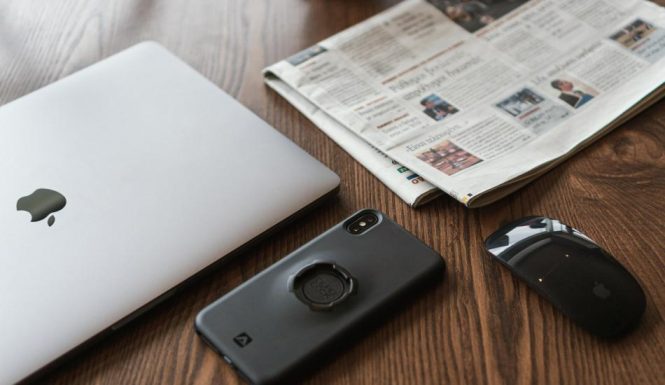 black smartphone on table next to laptop and newspaper