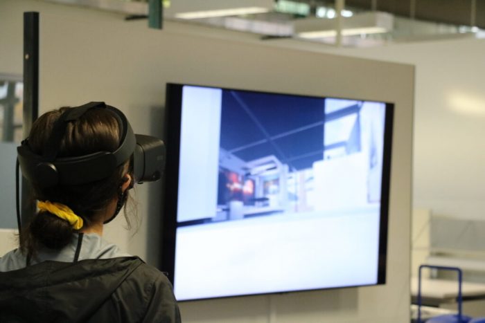 Female student wearing VR headset, large monitor in the background.