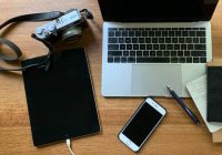 laptop, camera, tablet, iphone, pen and notepads arranged on tabletop