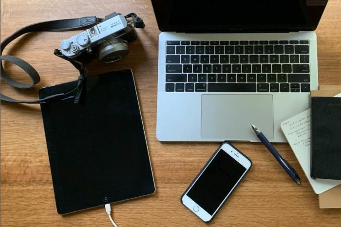 laptop, camera, tablet, iphone, pen and notepads arranged on tabletop