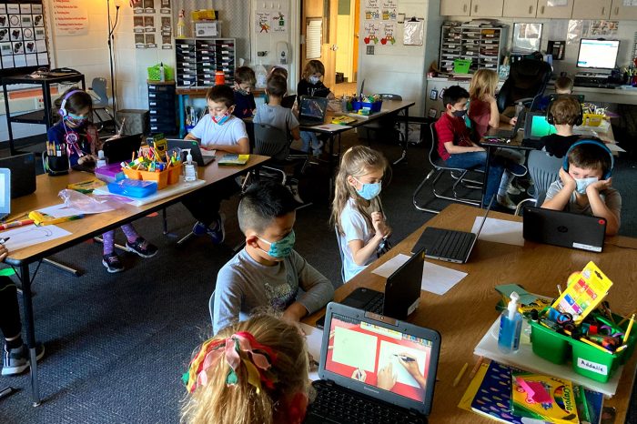 Classroom of masked children working on laptops.