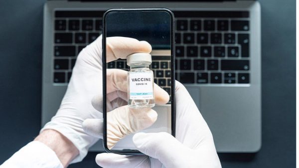 iphone taking photo of vaccine vial, laptop in BG