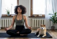 Young african american woman in apartment meditating, dog next to her.