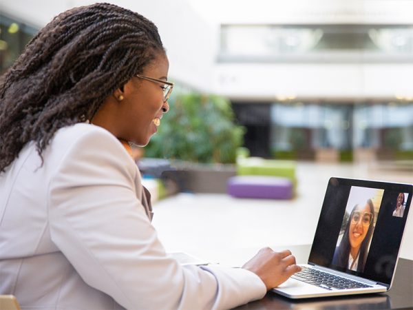 Profile of a business women using a laptop to talk with another woman through a video call. Both women are smiling.