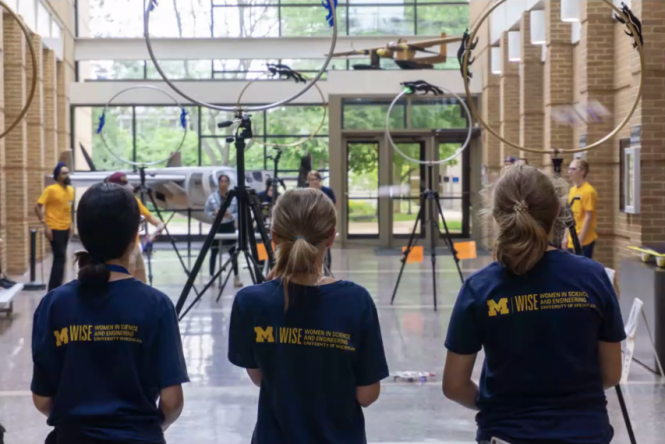 Three girls playing quadcopter quidditch in engineering building.