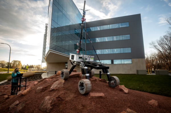 The Mars Rover is shown in a small hill with bumpy terrain. An engineer is off to the left. 