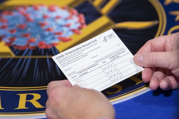 A Covid vaccination card is shown being held by two hands.