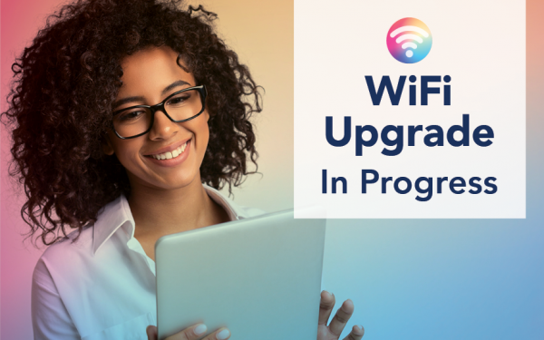 A Black woman in a white shirt wearing glasses is smiling while using her tablet. Text says WiFi Upgrade In Progress