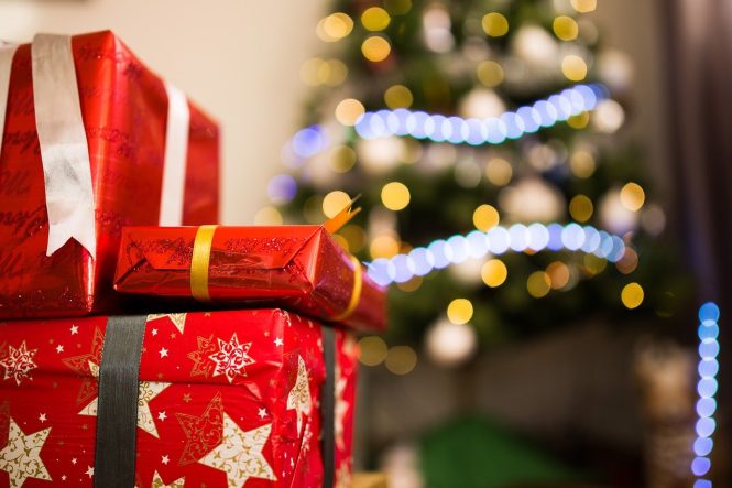 Gifts wrapped in metallic red paper with gold stars and gold ribbon. A Christmas tree is in the background.