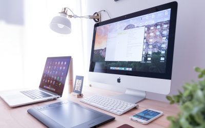 Multiple tech devices (laptop, desktop, tablet, phone, keyboard) and a lamp