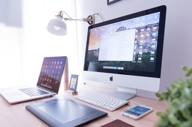 Multiple tech devices (laptop, desktop, tablet, phone, keyboard) and a lamp