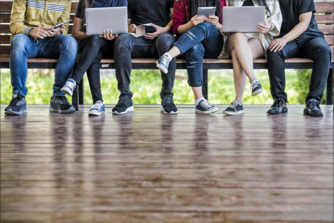 Six students sitting together on a bench outside with their laptops and mobile devices.