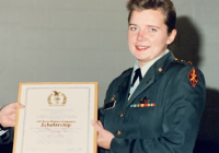 Liz Lind is pictured receiving an award. She is wearing her Army uniform and is holding a framed certificate.
