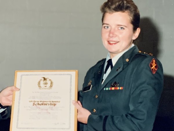 Liz Lind is pictured receiving an award. She is wearing her Army uniform and is holding a framed certificate. 