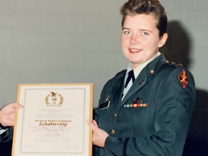 Liz Lind is pictured receiving an award. She is wearing her Army uniform and is holding a framed certificate.