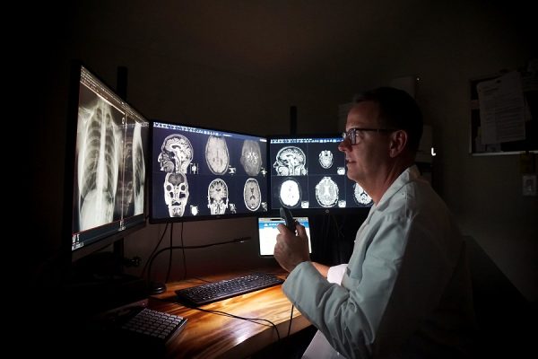 Dr. Todd sits in front of three computer monitors that have x-rays on them of lungs and brains.