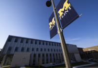 A building on UM-Flint's campus with two UM-Flint flags on a light pole out front.
