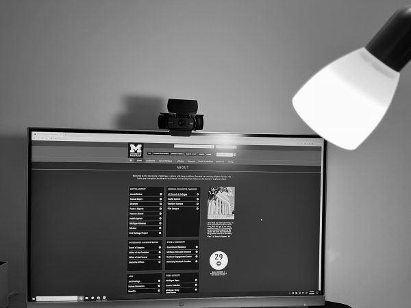 a black and white photo of a computer monitor showing the University of Michigan's about page, and a desk lap shining a light on the monitor.