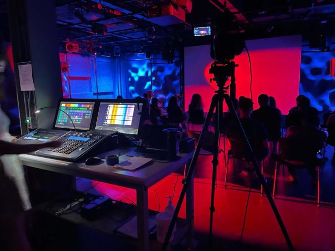 A control board is shown on the left. On the right are silhouettes of students and a tripod camera.