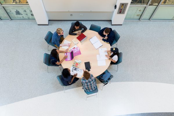 An arial view of seven students seated around a circular table, collaborating on some work.