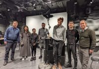 Members of the Visualizing Telematic Performance team stand on a stage after the December concert. From left to right are John Granzow, Rebecca Zhang, Sui Lin Tam, Matt Albert, Adam Schmidt, Gavin Ryan, and Michael Gurevich, with LARS the robot in the middle.