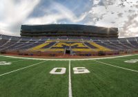 The Michigan Stadium - the perspective is on the field at the 50 yard line looking toward the bleachers and a partly sunny, partly cloudy sky.