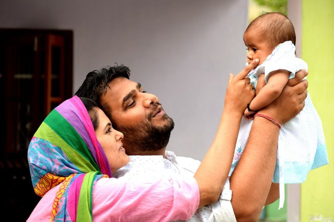 A mother and a father smile at their infant.