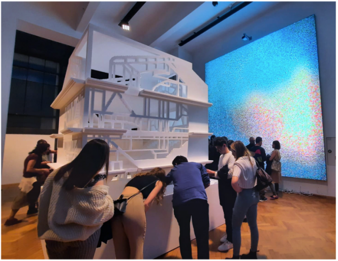 A very large 3D model of a house with students around it studying the details.