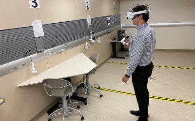 Person standing wearing VR goggles and controller, interacting with items on a wall.