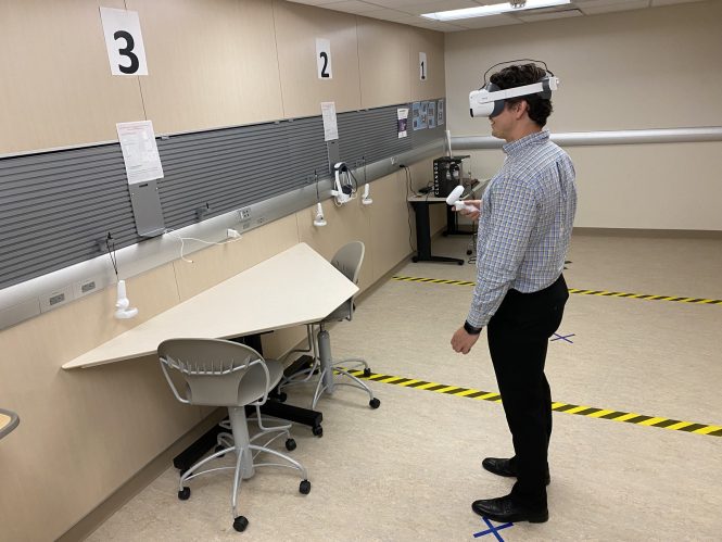 Person standing wearing VR goggles and controller, interacting with items on a wall.