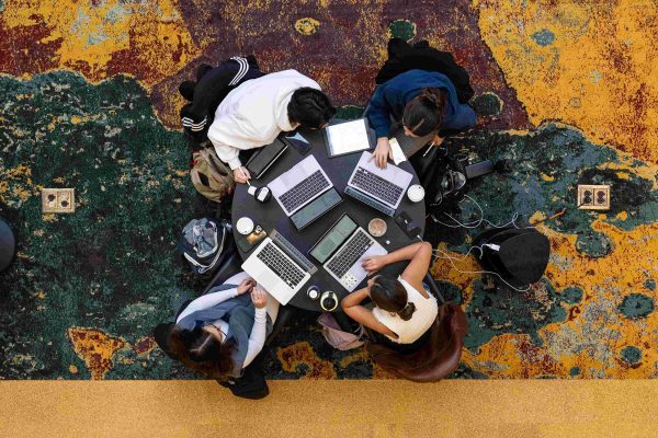 pictured from directly above, a group of 4 students sit at a round table with their laptops open