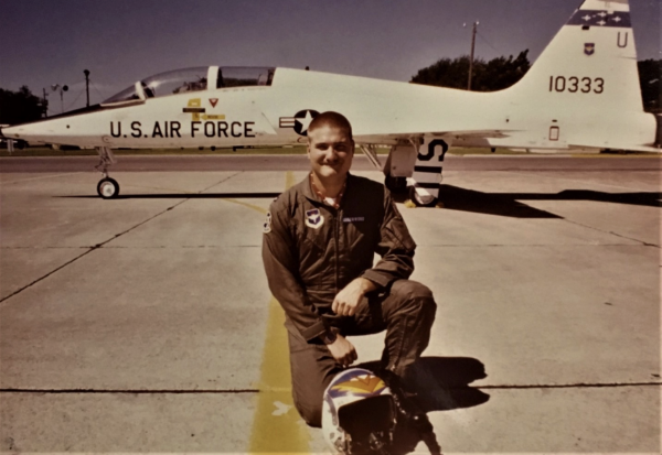 a young jack underwood kneels in front of an air force jet, the photo is slightly sepia toned