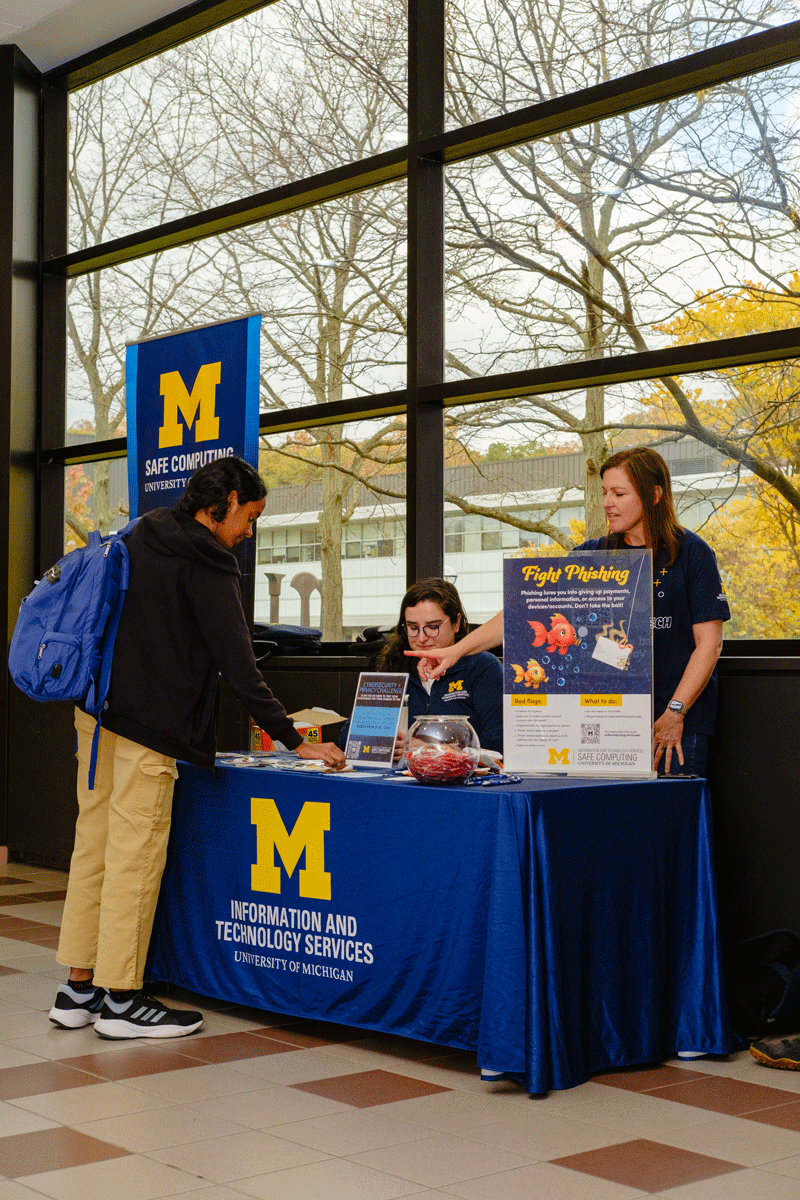 A student picks up pamphlets from an IA table at the Duderstadt Center