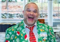 Joe Gregoria grinning at the camera in a Christmas-themed suit.