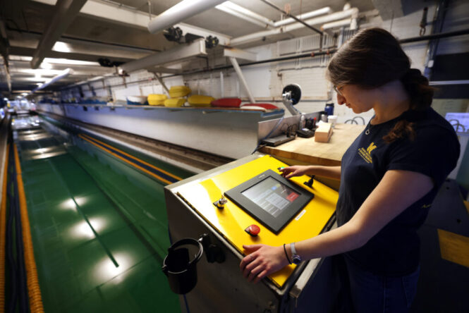 A woman operates a machine in the U-M Marine Hydrodynamics Lab, focused on her task amidst industrial equipment and tools.