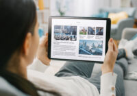 Over the Shoulder Shot of a Young Woman at Home Lying on a Couch and Using Tablet Computer in Horizontal Landscape Mode for Reading News about Technology.