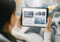 Over the Shoulder Shot of a Young Woman at Home Lying on a Couch and Using Tablet Computer in Horizontal Landscape Mode for Reading News about Technology.