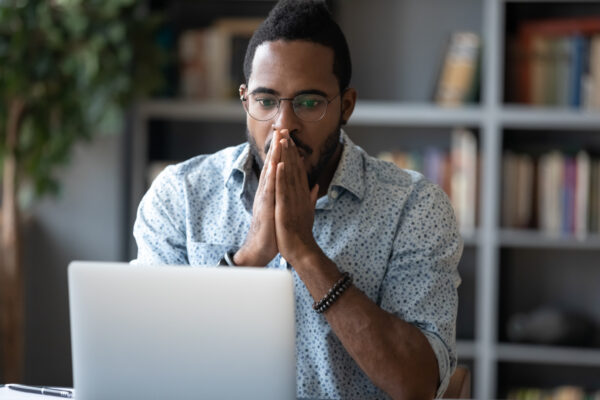 Shocked african business man looking at laptop feeling scared and frustrated about an unexpected online problem