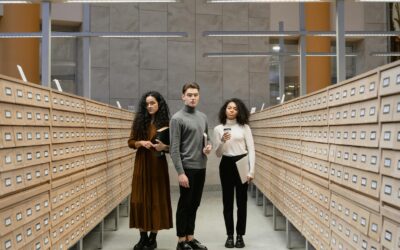 Three students browsing a card catalog aisle in a modern library setting.